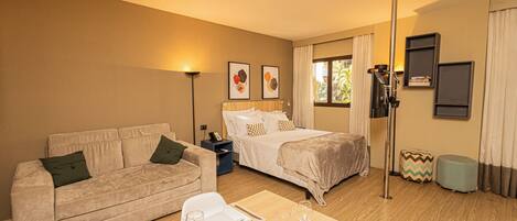 A hotel room with a bed, a sofa, a dining table set with plates and glasses, a lamp, and a window with curtains.