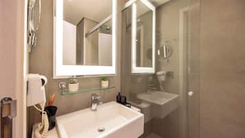 Un baño con lavamanos blanco, repisa de vidrio con una planta, espejo y cabina de ducha de vidrio.
