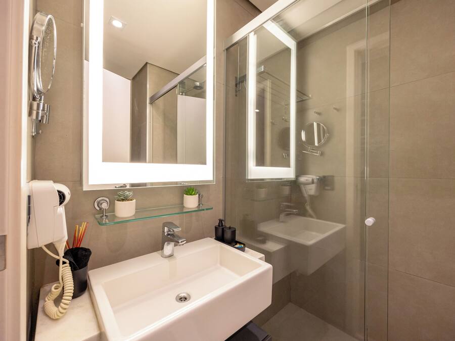 Un baño con lavamanos blanco, repisa de vidrio con una planta, espejo y cabina de ducha de vidrio.
