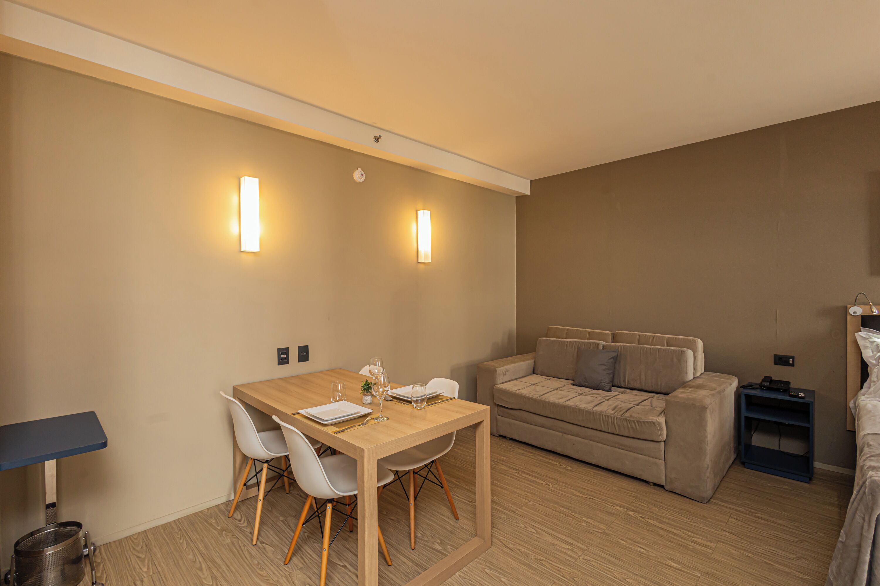 A modern room with a wooden dining table, white chairs, a beige sofa, and a small side table.