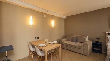 A modern room with a wooden dining table, white chairs, a beige sofa, and a small side table.