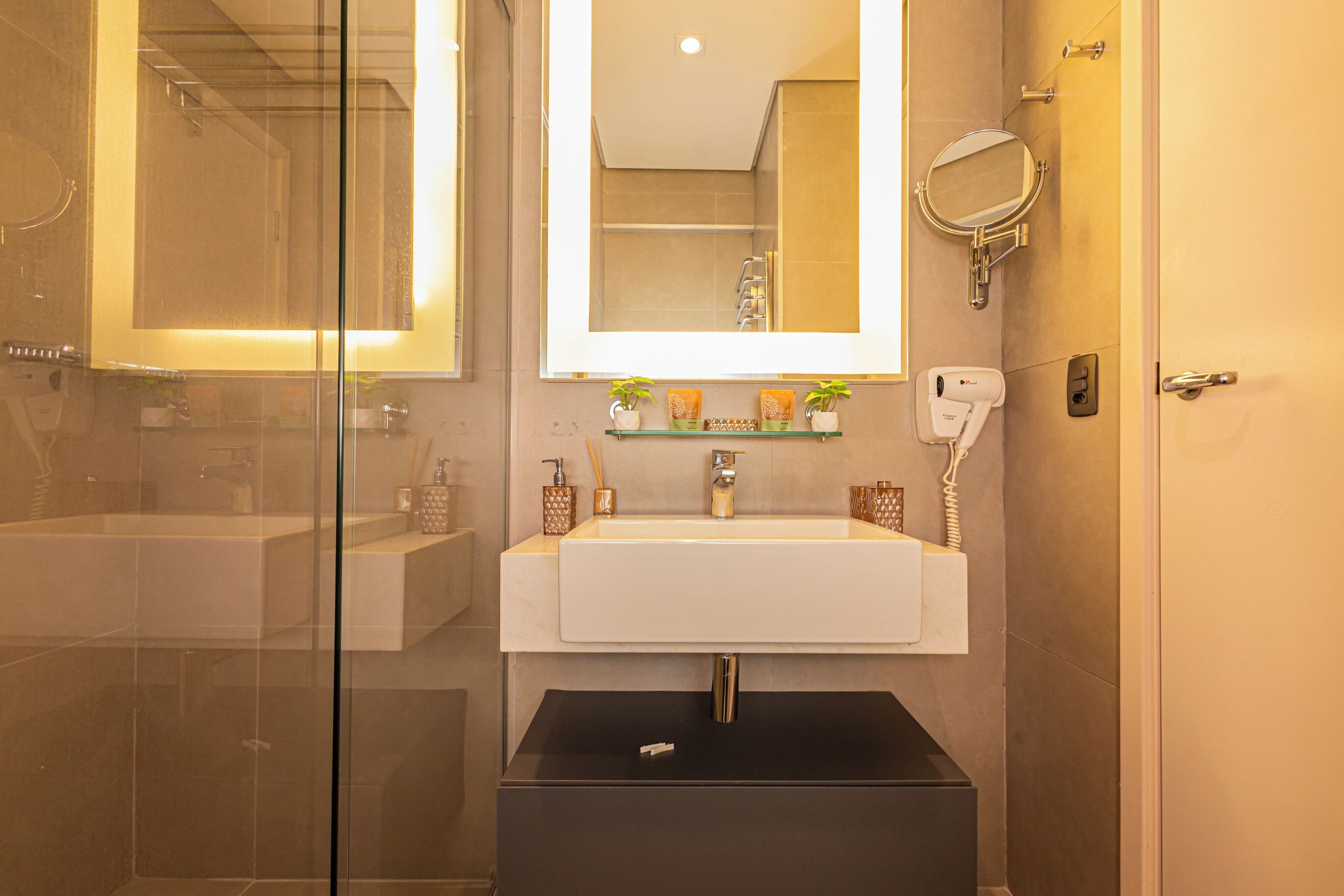Un baño moderno con cabina de ducha de vidrio, un lavabo blanco con espejo arriba y un mueble negro debajo.