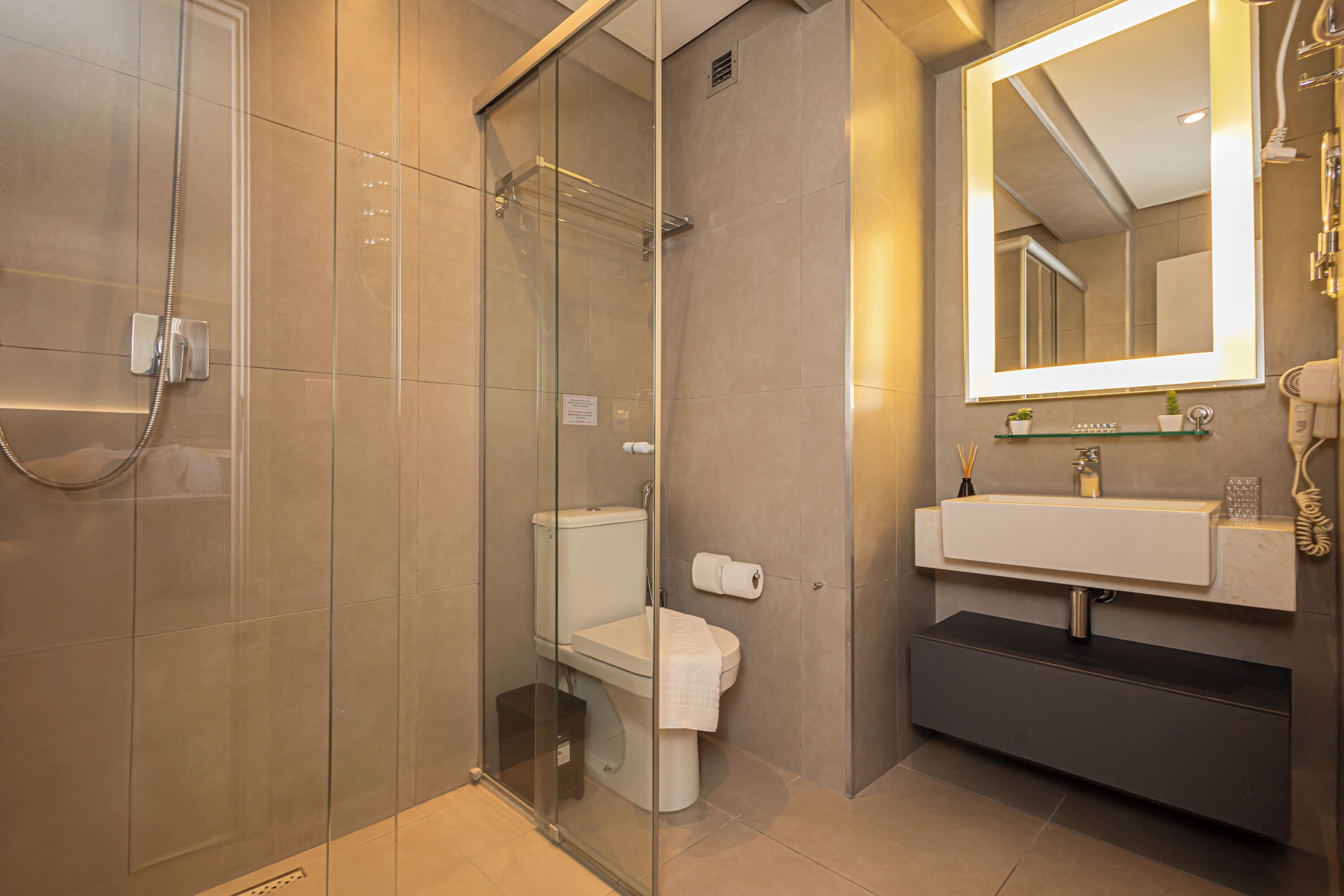 Un baño moderno con ducha de vidrio, inodoro, lavamanos con espejo y perchero para toallas.