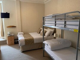 Een hotelkamer met stapelbedden, een nachtkastje met lamp, een aan de muur bevestigde televisie en een klein houten plankje.