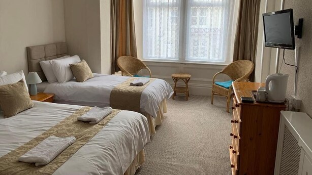 A hotel room with two beds, a small table, a chair, a television, and a window with curtains.