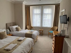 Camera d'albergo con due letti, un tavolino, una sedia, un televisore e una finestra con tende.
