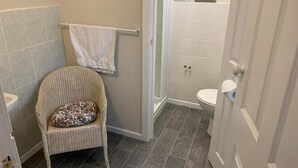 A bathroom with a wicker chair, a towel rack, a shower, and a toilet.