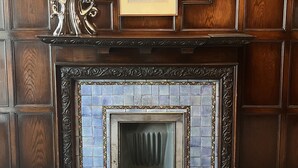 A fireplace with a tiled surround, a framed picture above it, and a decorative metal piece on the mantel.