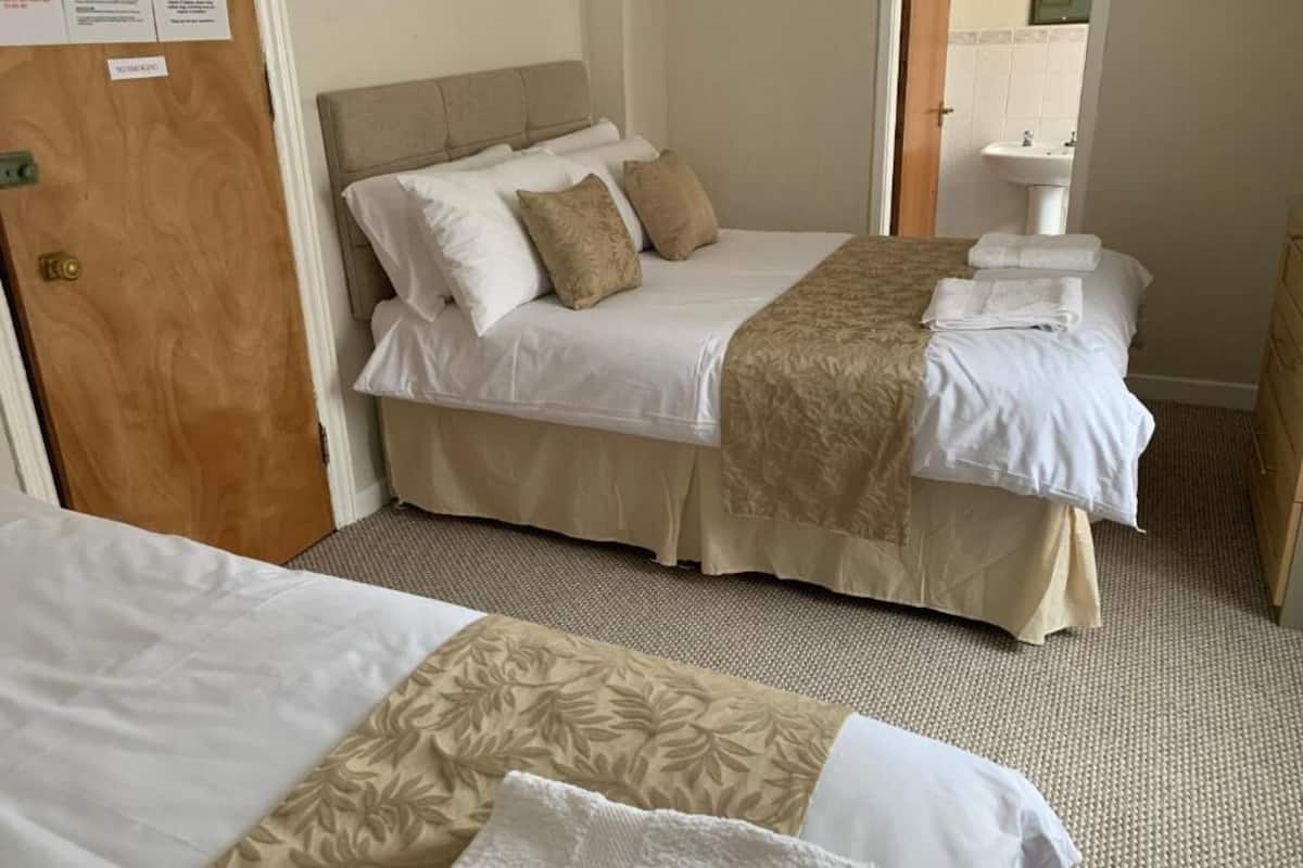 A hotel room with two beds, a wooden door, a sink, and a mirror.