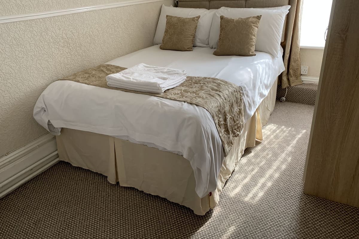 A neatly made bed with a white and beige bedspread, two pillows, and a folded white towel.