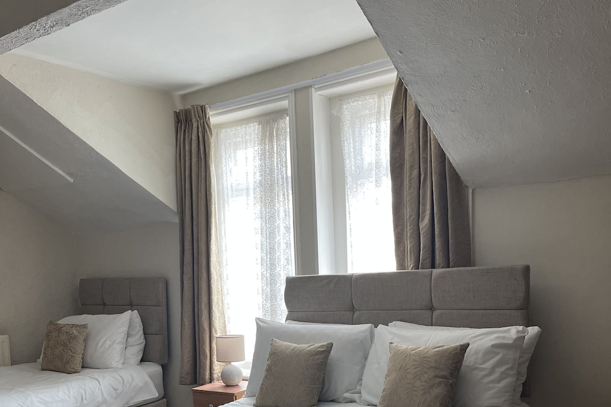 A hotel room with two beds, a large window with curtains, and a ceiling with exposed beams.