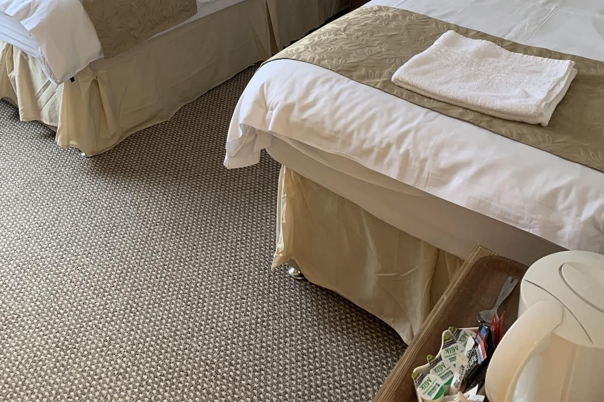 Two twin beds with beige bedding, a nightstand with a lamp, and a small table with a remote control.