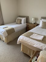 Two twin beds with beige bedding, a nightstand with a lamp, and a small table with a remote control.