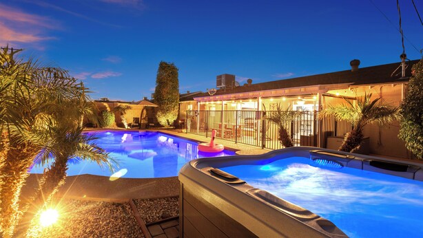 Une piscine avec un jacuzzi, entourée de palmiers et bordée d’un bâtiment doté d’une terrasse couverte.