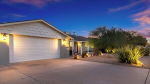 Une maison d’habitation avec un garage, une véranda et un jardin aménagé avec des cactus et des rochers.