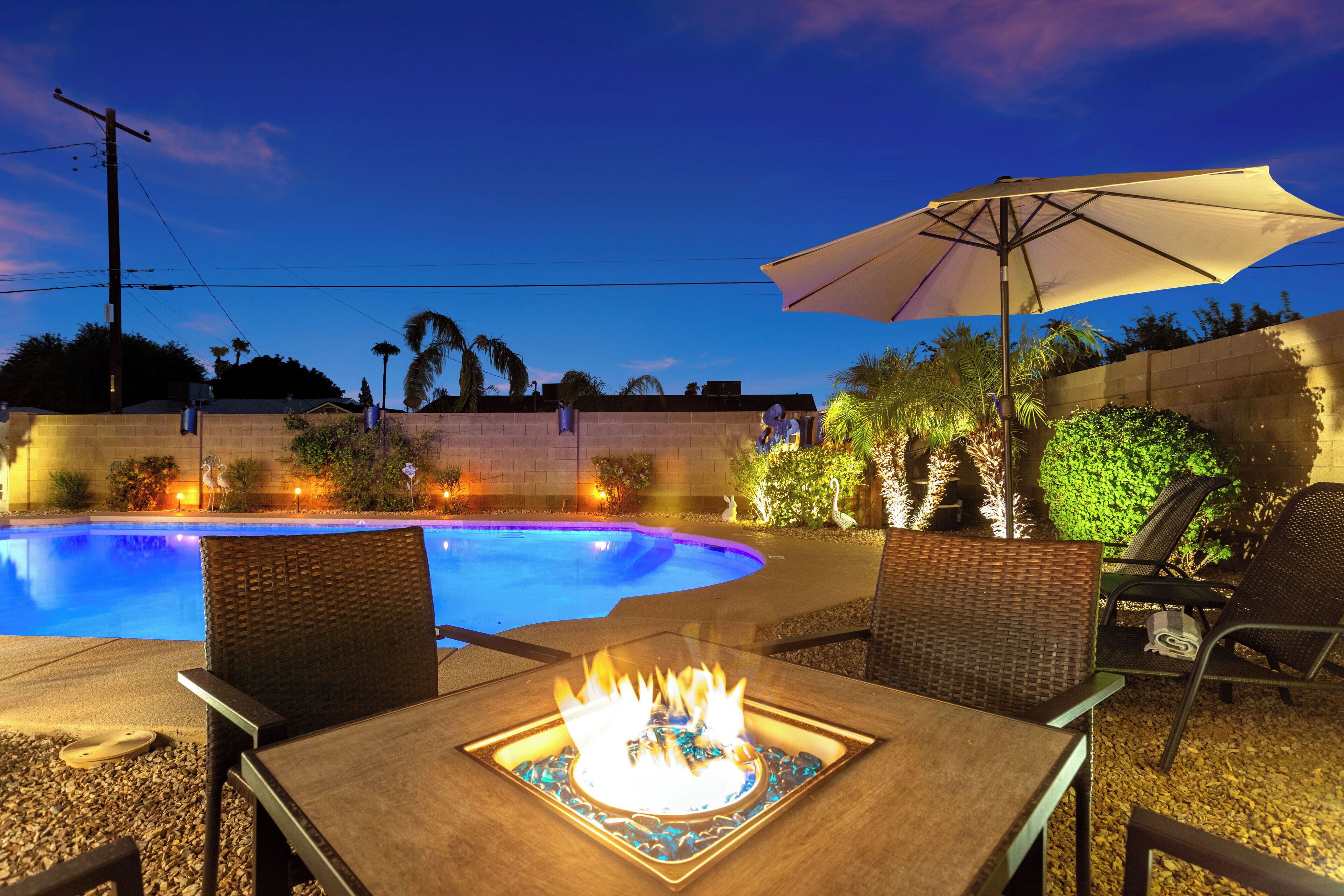 An outdoor pool area with a fire feature, seating, and an umbrella.