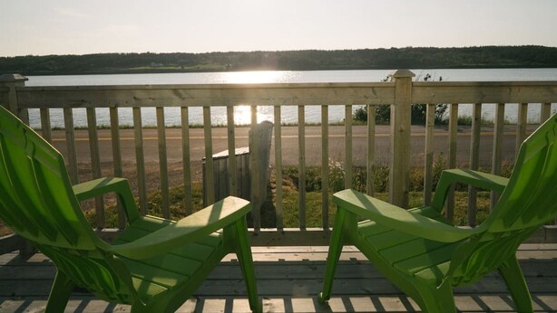 Une terrasse en bois avec deux chaises vertes donnant sur un lac.
