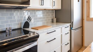 A kitchen with a black stove, white cabinets, and a stainless steel refrigerator. - Beach, Beach, Beach - Cabaneaux 1 (Chéticamp)