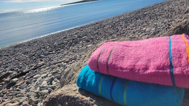 A rocky beach with a clear view of the water and a pile of colorful towels. - Beach, Beach, Beach - Cabaneaux 1 (Chéticamp)