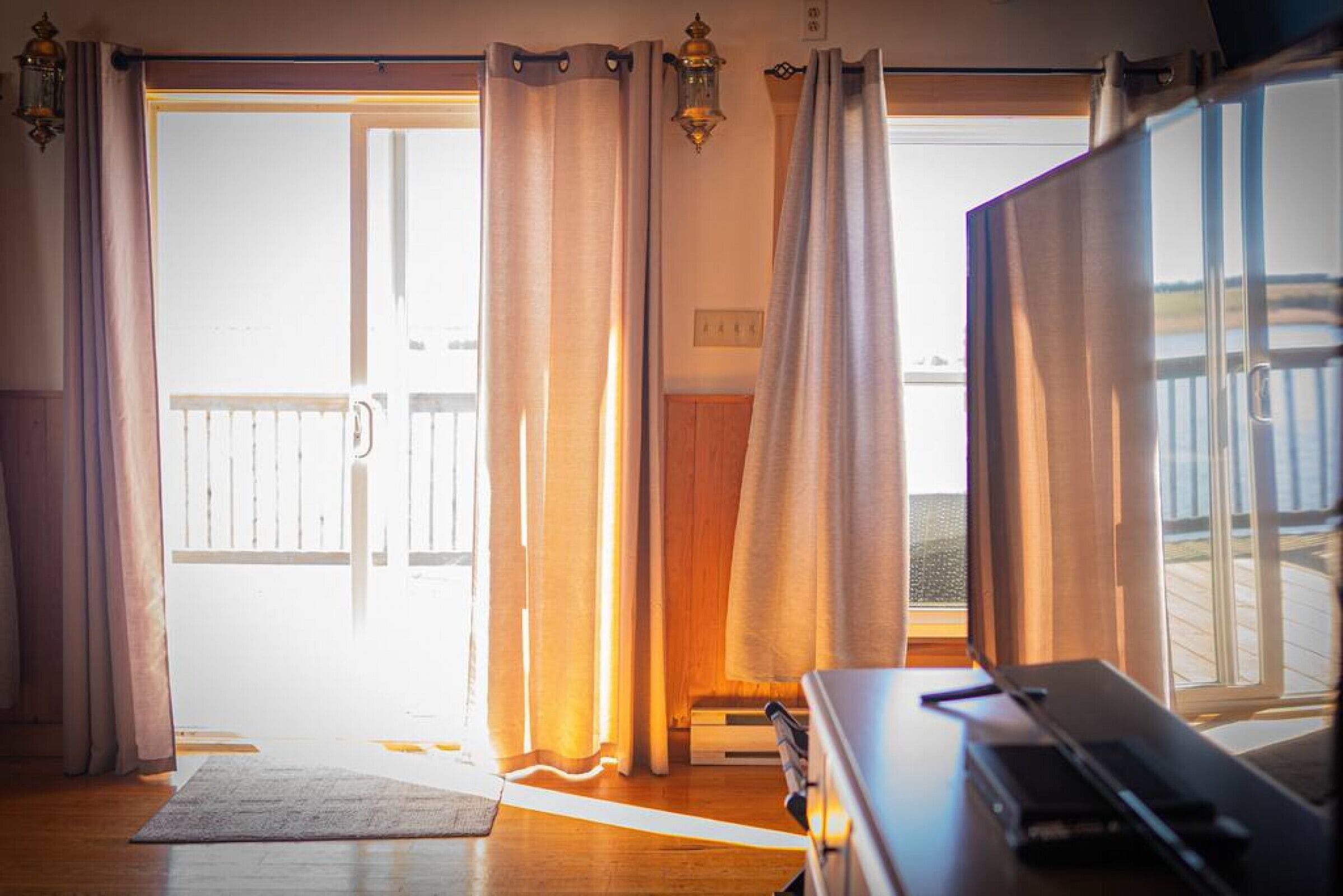 Una habitación con puerta corrediza de vidrio que da a un balcón, un escritorio de madera con una computadora portátil y una pequeña alfombra en el suelo.