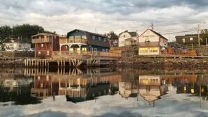 A waterfront property with multiple buildings, including a large house with a balcony and a smaller structure. - The most wanted place to stay in Cheticamp (Chéticamp)