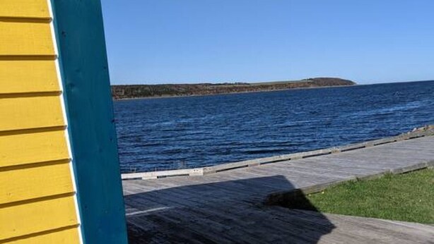 A wooden boardwalk leading to a body of water with a distant landmass. - Tiny home on the Boardwalk (Chéticamp)