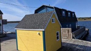 A yellow and blue house with a dock extending into a body of water. - Tiny home on the Boardwalk (Chéticamp)