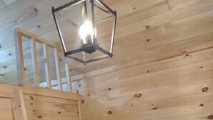 A wooden cabin interior with a wooden ladder, a black sofa, and a hanging light fixture. - Tiny home on the Boardwalk (Chéticamp)