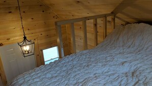 A bedroom with a wooden ceiling, a bed with a white quilt, and a hanging lantern. - Tiny home on the Boardwalk (Chéticamp)
