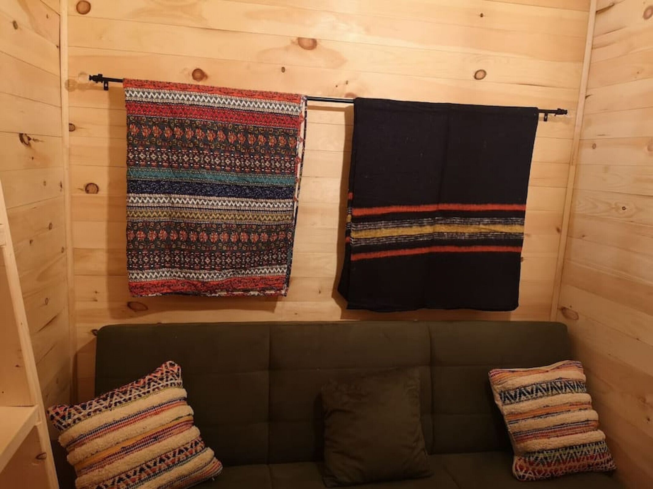 A wooden cabin interior with a sofa and two patterned blankets hanging on the wall.