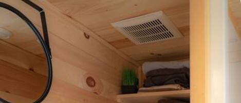 A compact wooden bathroom with a toilet, a sink, and a small shelf with toiletries.
