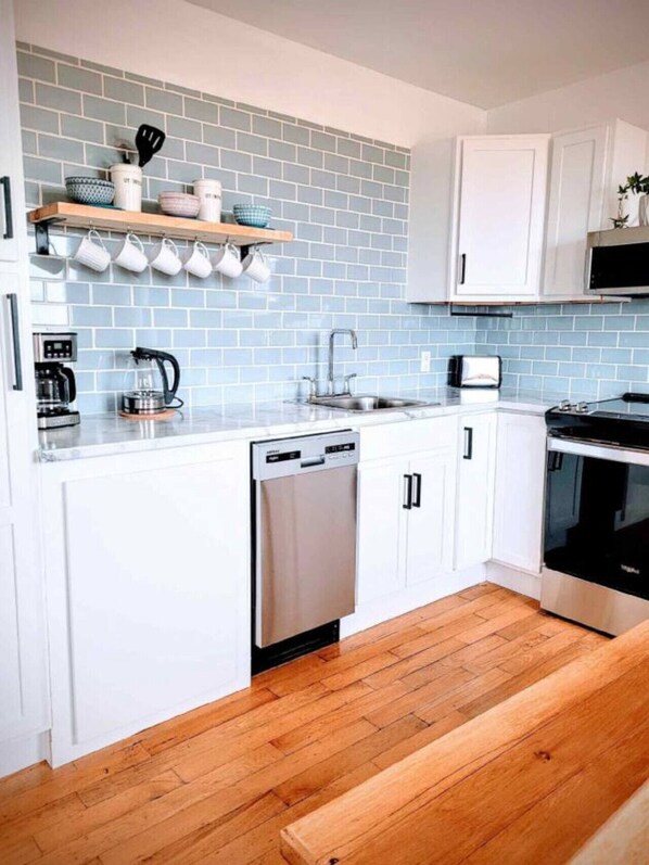 Une cuisine moderne avec des meubles blancs, un lave-vaisselle, un four à micro-ondes et un plan de travail en bois.