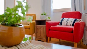A living room with a red armchair, a yellow armchair, a wooden cabinet, and a potted plant. - Sunsets, barbecue`s and sandy beach - Cabaneaux 4 (Chéticamp)