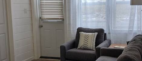 A living room with a gray sofa, a wooden coffee table, and a door with white blinds.