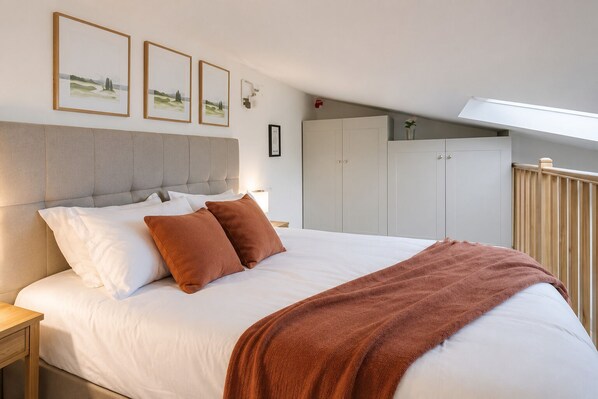 A bedroom with a large bed, a headboard, a nightstand, and a wardrobe.