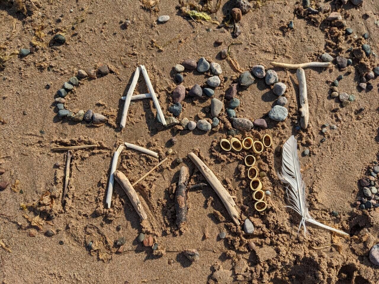 A sandy beach with rocks and sticks arranged to spell "CASOT".