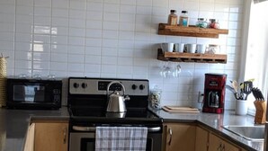 Une cuisine équipée d’une cuisinière en acier inoxydable, d’un four à micro-ondes, de meubles en bois et d’une fenêtre avec des stores.