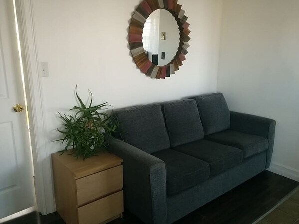 A living room with a grey sofa, a wooden side table with a plant, and a wall-mounted mirror. - The Upperdeck o the ocean (Chéticamp)