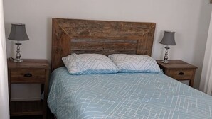 Une chambre à coucher avec une tête de lit en bois, deux tables de chevet avec des lampes et un lit recouvert d’une couvre-lit bleue à motifs.