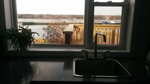 Une cuisine équipée d’un évier et d’une fenêtre donnant sur un quai et l’eau.