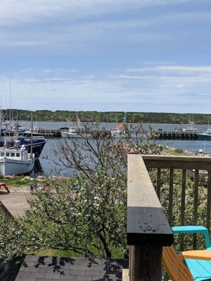 A marina with boats docked, a wooden deck, and a view of the water and greenery in the background. - The Upperdeck o the ocean (Chéticamp)