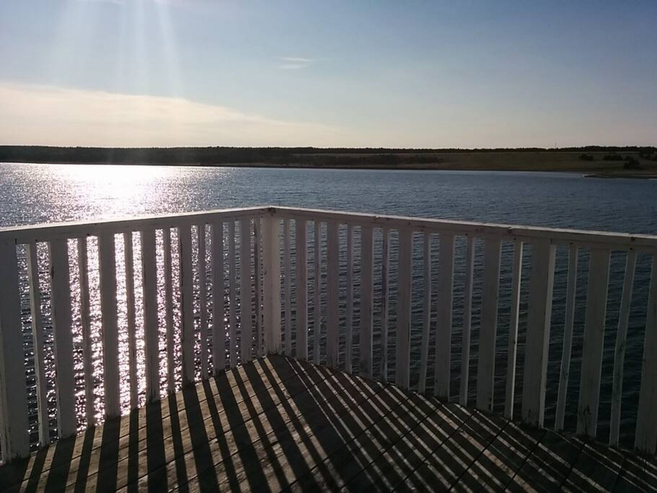 Een houten terras met een balustrade, met uitzicht op een rustig wateroppervlak.
