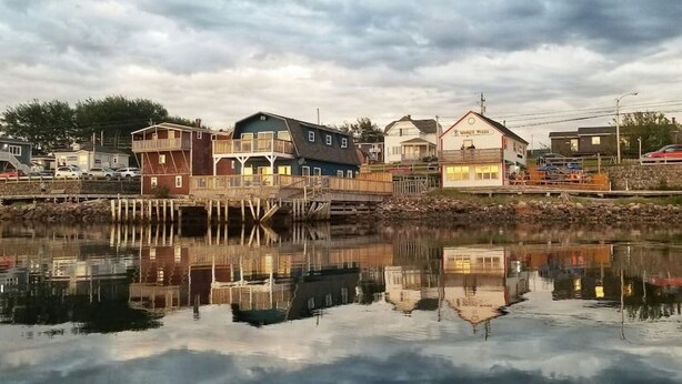 Um imóvel à beira-mar com um cais, um edifício com varanda e uma pizzaria do outro lado da água.