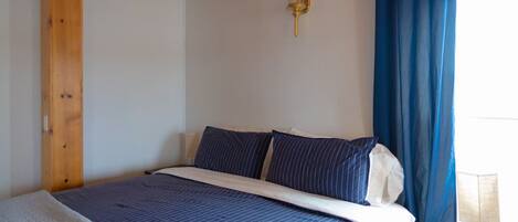 Une chambre à coucher avec un lit, des rideaux bleus, une lampe fixée au mur et un plafond en bois.