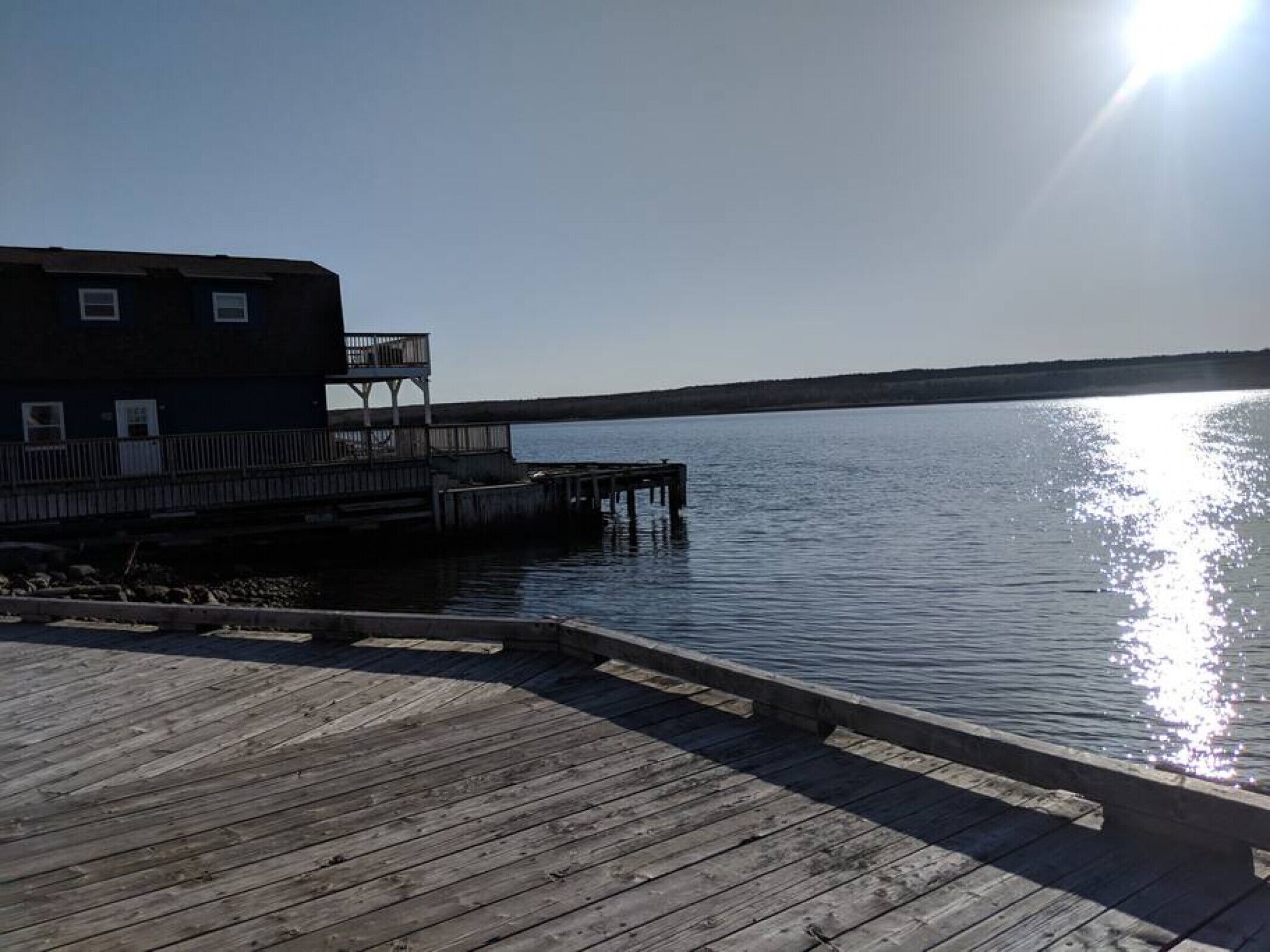 A wooden pier extending into calm water, with a building featuring a balcony on the left.