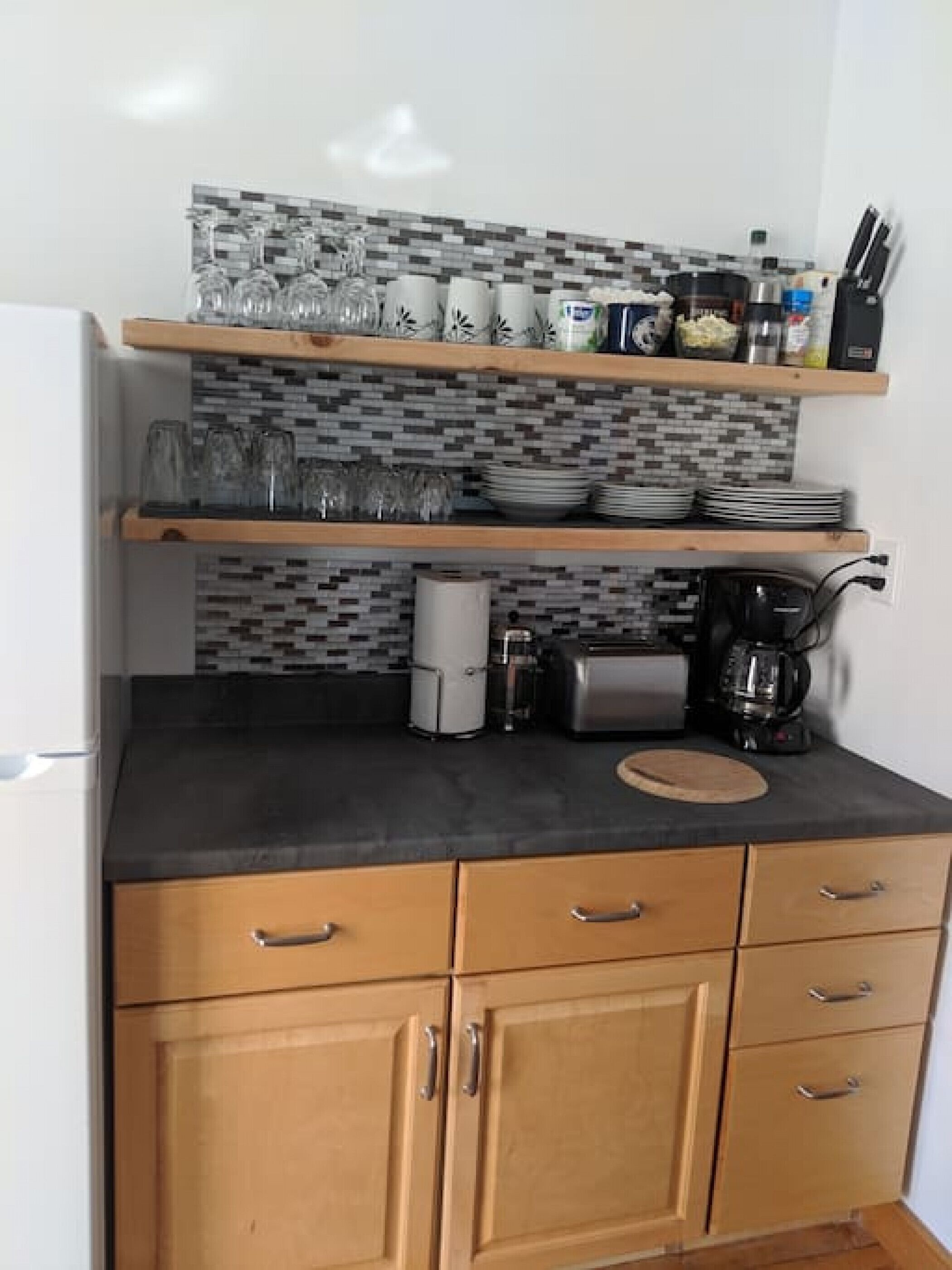 A kitchen with a black countertop, wooden cabinets, a coffee maker, and a tiled backsplash.
