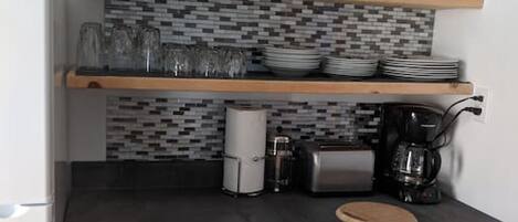 A kitchen with a black countertop, wooden cabinets, a coffee maker, and a tiled backsplash.