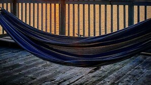 Uma rede sobre um deck de madeira com vista para o pôr do sol sobre a água.