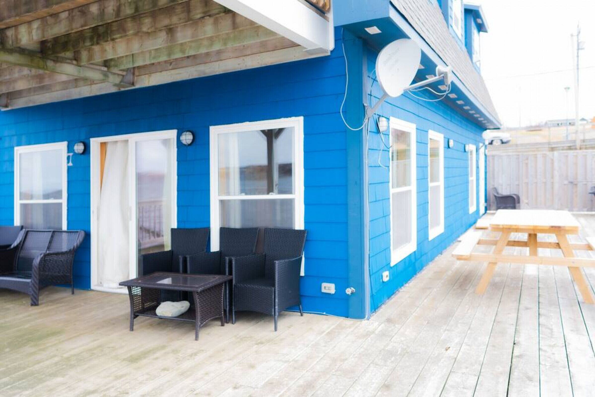 Ein blaues Gebäude mit einer überdachten Terrasse, ausgestattet mit Korbmöbeln und einem Holztisch.