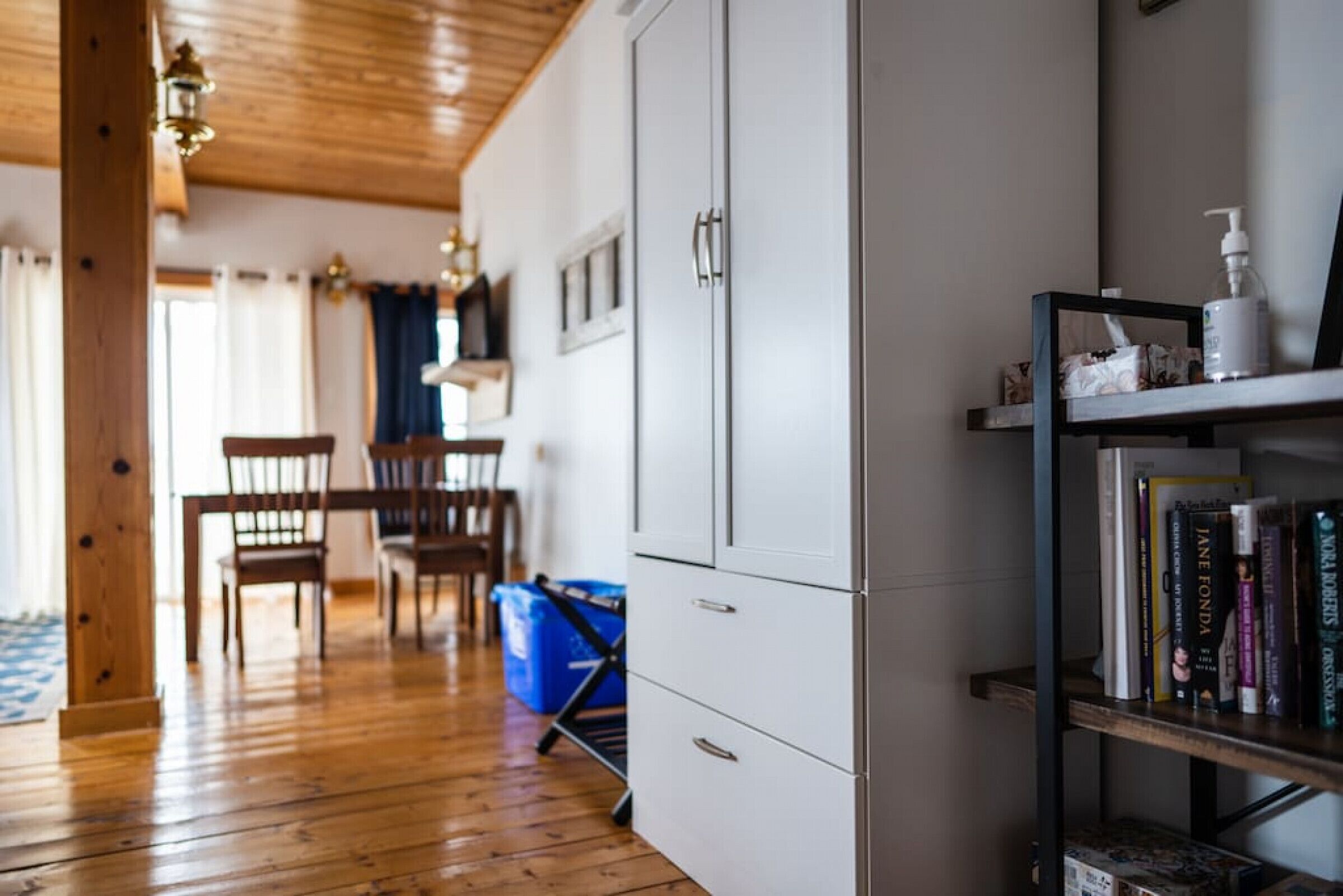 Ein Zimmer mit Holzboden, einem weißen Schrank, einem Bücherregal und einer Essecke mit Stühlen und einem Tisch.